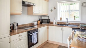 A modern kitchen with white cabinets, a stainless steel range, a microwave, and a sink. - Bullions Farm Cottage (Consett)