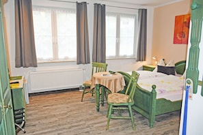A room with a bed, a table with chairs, a window with curtains, a radiator, and a painting on the wall. - 02 Double room incl. breakfast - Bed and breakfast in Sellin (Sellin)