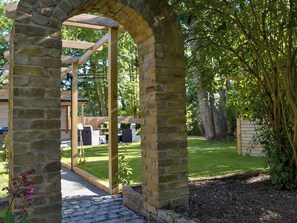 Un arco in pietra che conduce a un pergolato di legno con posti a sedere all'aperto.