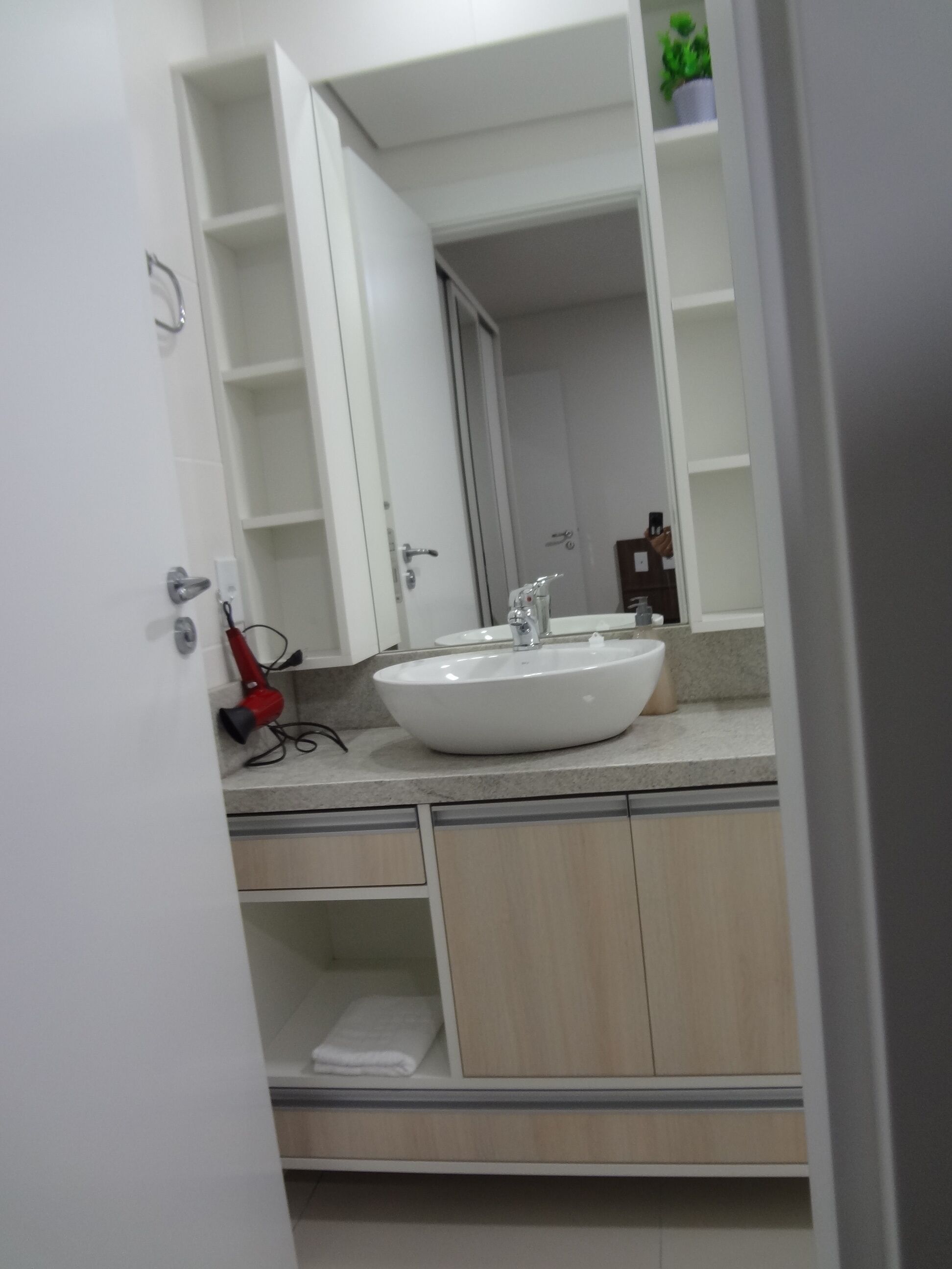Un baño con un lavamanos blanco, un espejo y un secador rojo sobre la encimera.