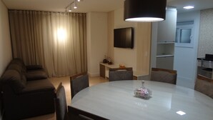 Una sala de estar moderna con una mesa de comedor redonda, un sofá, un televisor y una zona de cocina.