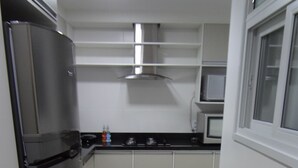 Una cocina con refrigerador de acero inoxidable, gabinetes blancos, microondas y estufa a gas.