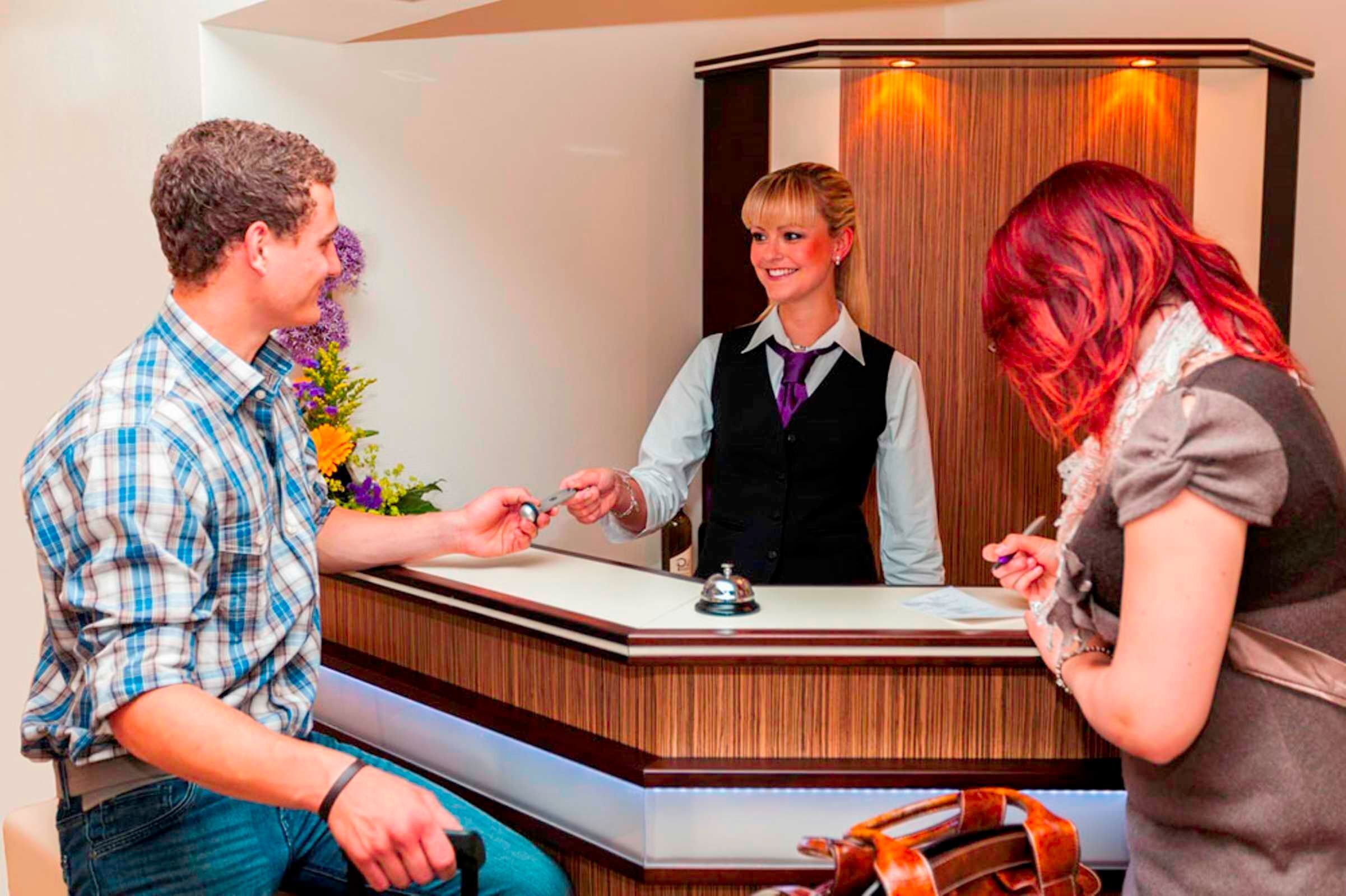 Ein Hotelrezeptionstresen mit einer Holztischplatte, einer Glocke und einer Blumenkomposition.