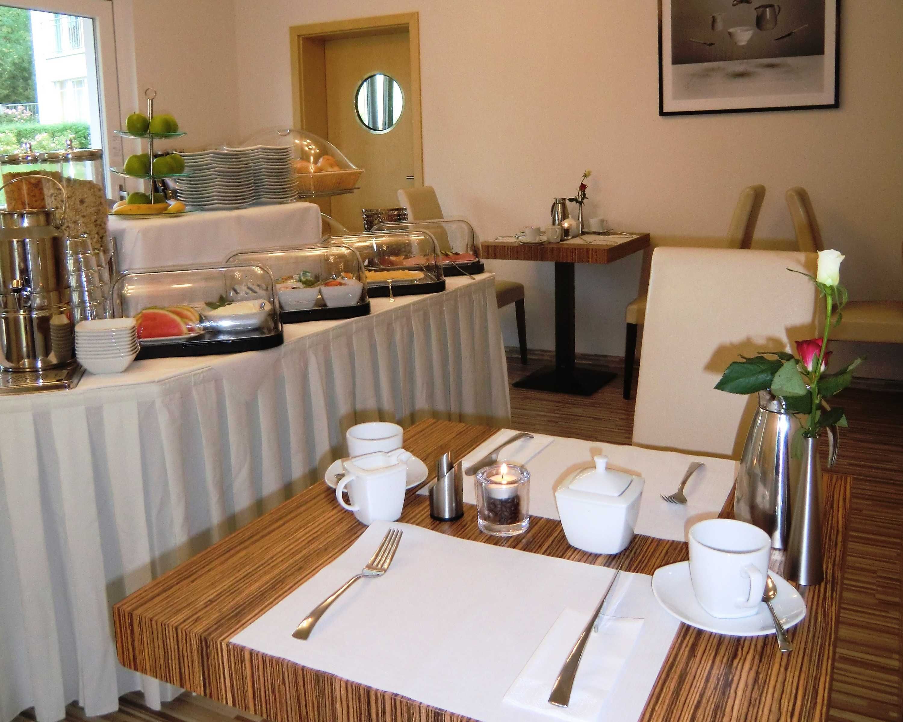 Ein reichhaltiges Frühstücksbuffet mit verschiedenen Speisen und ein Esstisch für zwei Personen, gedeckt mit Besteck und Tassen.