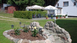 Un hotel con mesas al aire libre, un jardín con rosales y un muro de piedra.