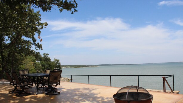 An outdoor patio with a table and chairs, a fire pit, and a view of a lake. - PRIVATE, SECLUDED LAKEFRONT RETREAT WITH BOAT DOCK, LARGE PATIOS AND HOT TUB!! (Runaway Bay)