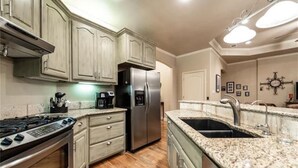 A kitchen with wooden cabinets, a stainless steel refrigerator, a gas stove, and granite countertops. - PRIVATE, SECLUDED LAKEFRONT RETREAT WITH BOAT DOCK, LARGE PATIOS AND HOT TUB!! (Runaway Bay)