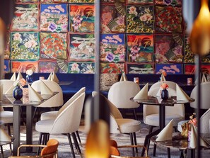 Interior de un restaurante con mesas, sillas y un llamativo mural colorido.