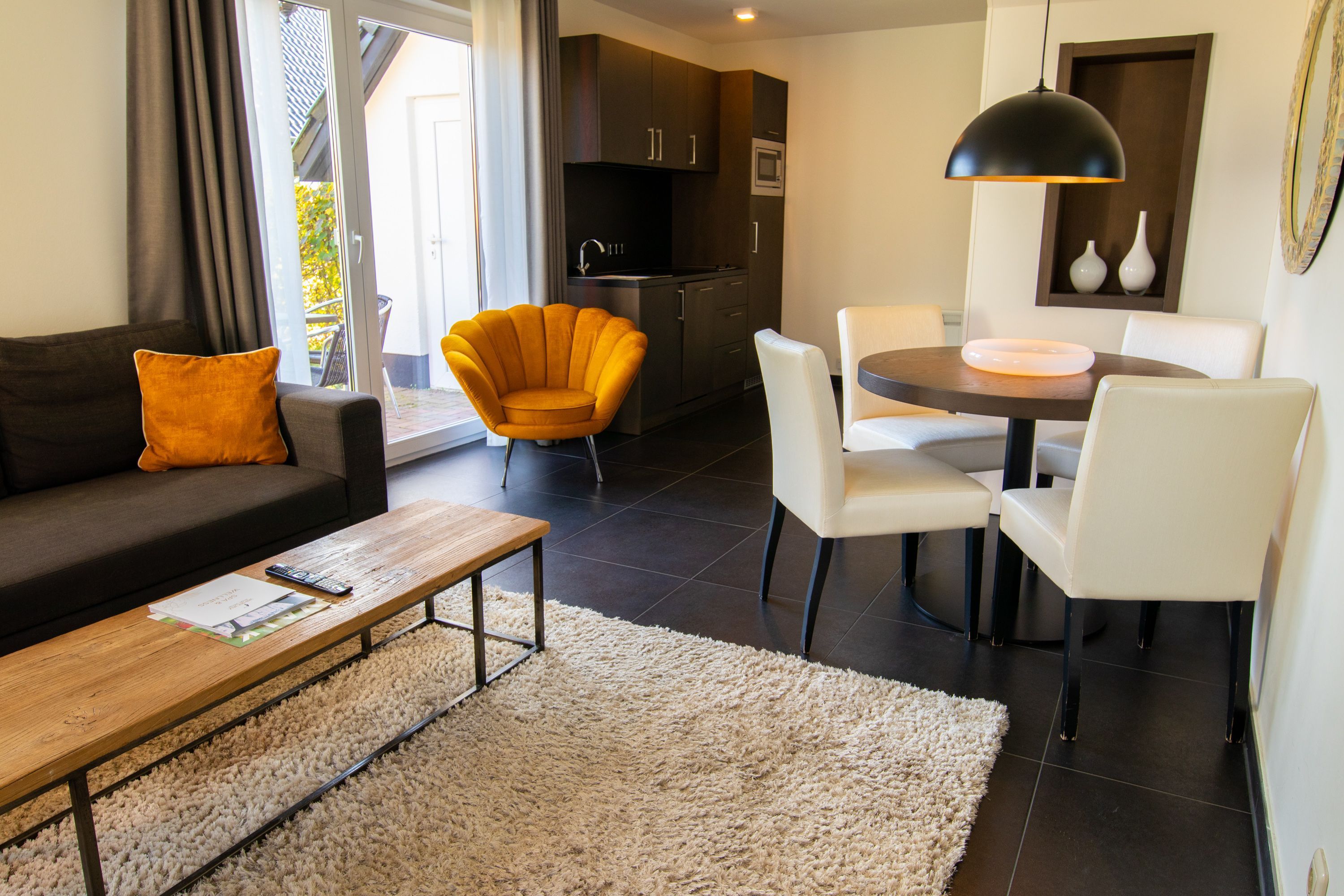 Een moderne woonkamer met een bank, fauteuil, salontafel, en een eethoek met stoelen en een tafel.