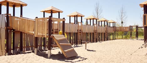 Una estructura de juego de madera en una playa arenosa, con varios niveles y toboganes.
