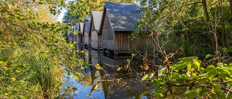A row of wooden cabins with metal roofs, surrounded by dense foliage and a calm body of water.