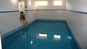Een klein binnenzwembad met betegelde wanden en een blauwe rand, een trap en een klok aan de muur.