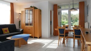 Een moderne woonkamer met een bank, een eettafel met stoelen, een kast en een groot raam met gordijnen.