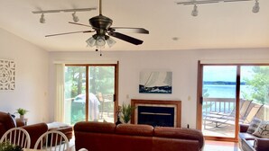 A spacious living room with a fireplace, a ceiling fan, and a view of a lake through large sliding glass doors. - Sunset Pines Retreat Castle Rock Lake (Arkdale)