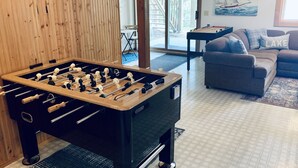A foosball table in a room with a wooden wall, a gray couch, and a painting of a sailboat. - Sunset Pines Retreat Castle Rock Lake (Arkdale)