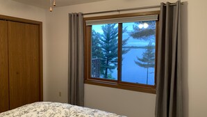 A bedroom with a bed, a window with curtains, a ceiling fan, and a view of trees and water. - Sunset Pines Retreat Castle Rock Lake (Arkdale)
