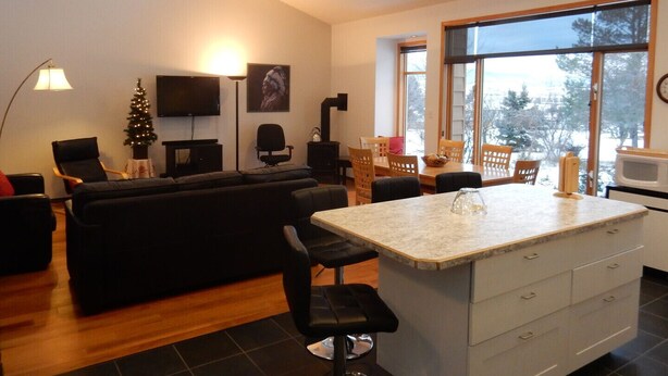 Una sala de estar moderna con un sofá negro, una mesa de centro y un televisor. Hay un comedor con una mesa y sillas, y una zona de cocina con un microondas.