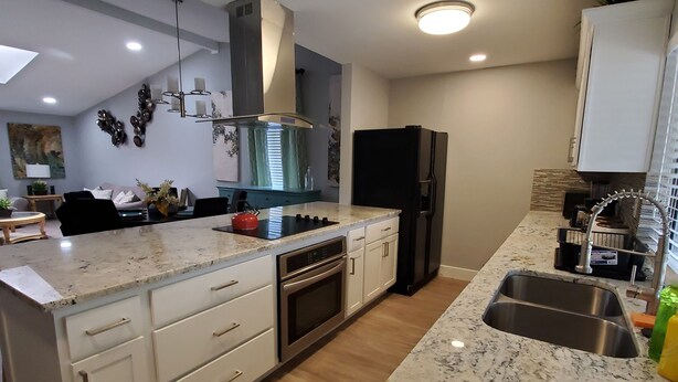A modern kitchen with white cabinetry, a black refrigerator, and a granite countertop. - Sharnu's Palace (DeSoto)