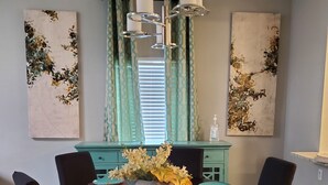 A dining area with a round table, black chairs, teal-colored cabinets, and abstract wall art. - Sharnu's Palace (DeSoto)