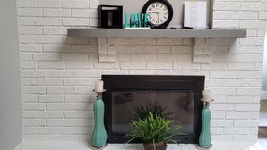 A fireplace with a flat-screen TV above it, a clock, and decorative items on the mantel. - Sharnu's Palace (DeSoto)