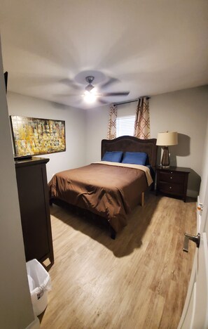 Une chambre à coucher avec un lit, un ventilateur de plafond, une table de chevet avec une lampe et un tableau accroché au mur.