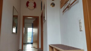 Een gang met een houten bankje, een reddingsboei aan de muur en een deur die leidt naar een balkon.