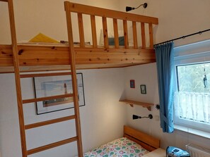 Un lit superposé avec une échelle en bois, une petite table de chevet, une lampe et une fenêtre avec des rideaux.