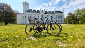 Een kasteelachtig gebouw met een toren, twee fietsen die er voor geparkeerd staan, en een gazon.