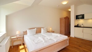 Een slaapkamer met een bed, nachtkastjes, een houten garderobe en een kitchenette.