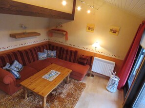 Un salon chaleureux avec un canapé en bois, une table basse en bois et un radiateur. On y trouve des coussins sur le canapé, une lampe et un cadre photo accroché au mur.