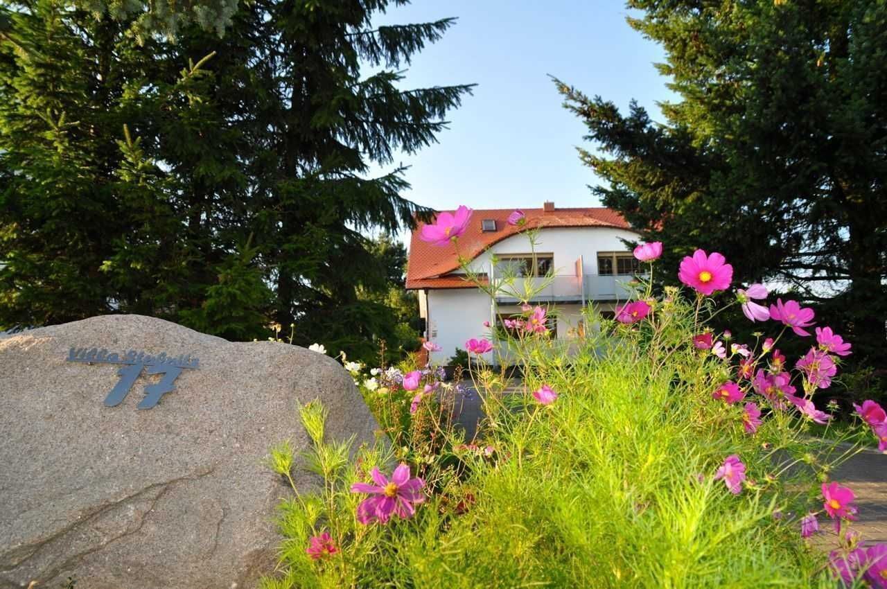 A building with a red roof, surrounded by lush greenery and pink flowers.