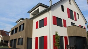 A modern two-story building with red shutters and a flat roof.