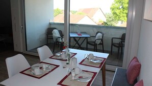 A dining area with a table set for four, chairs, a small table with a vase, and a view of the outside.