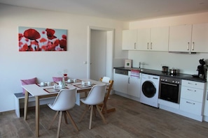 Une cuisine moderne avec des meubles blancs, un lave-linge et un coin repas comprenant une table et des chaises.