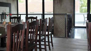 A dining area with wooden chairs and a table, large windows with a view of buildings, and a metal gate leading outside.