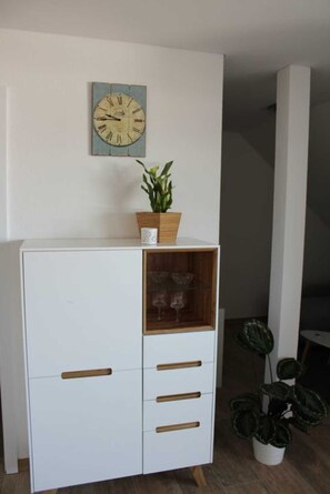 Un meuble blanc avec des poignées en bois, une horloge au mur et une plante en pot posée sur le dessus.