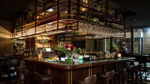 A bar area with multiple shelves of bottles and glasses, a central bar counter with stools, and a decorative vase with flowers. - Grand Canal Dock Waterfront Luxury “Special Offer” (Dublin)