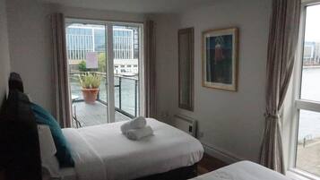 Habitación de hotel con dos camas, una planta en maceta, un cuadro y vistas al exterior.