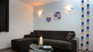 Un salon avec un canapé gris, une table basse en verre, une bougie allumée et deux lampes fixées au mur.
