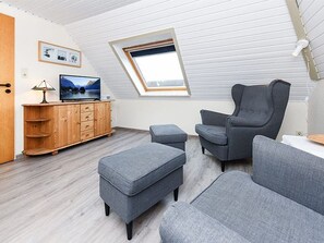A modern loft-style room with a sloped ceiling, a skylight, a wooden cabinet, a grey sofa, and a television.