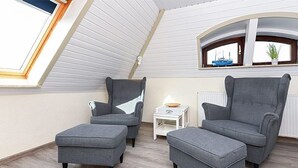 A room with a sloped ceiling, two grey armchairs, a small white table, and a radiator. - Apartment 8 - Haus Störtebeker (Neuharlingersiel)