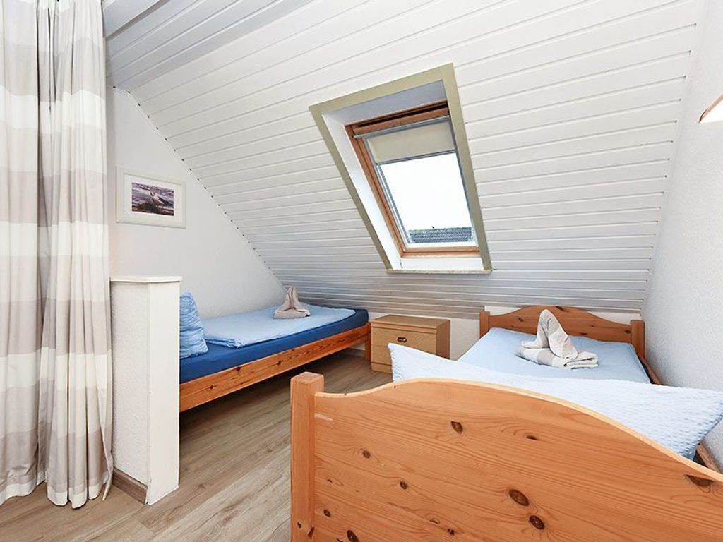 Ein Schlafzimmer mit geneigter Decke, einem Oberlicht, einem hölzernen Bett, einem Nachttisch und einer kleinen Nachttischlampe.