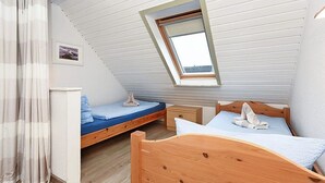 A bedroom with a sloped ceiling, a skylight, a wooden bed, a bedside table, and a small bedside lamp. - Apartment 8 - Haus Störtebeker (Neuharlingersiel)