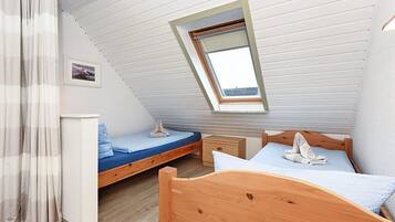 Ein Schlafzimmer mit geneigter Decke, einem Oberlicht, einem hölzernen Bett, einem Nachttisch und einer kleinen Nachttischlampe.