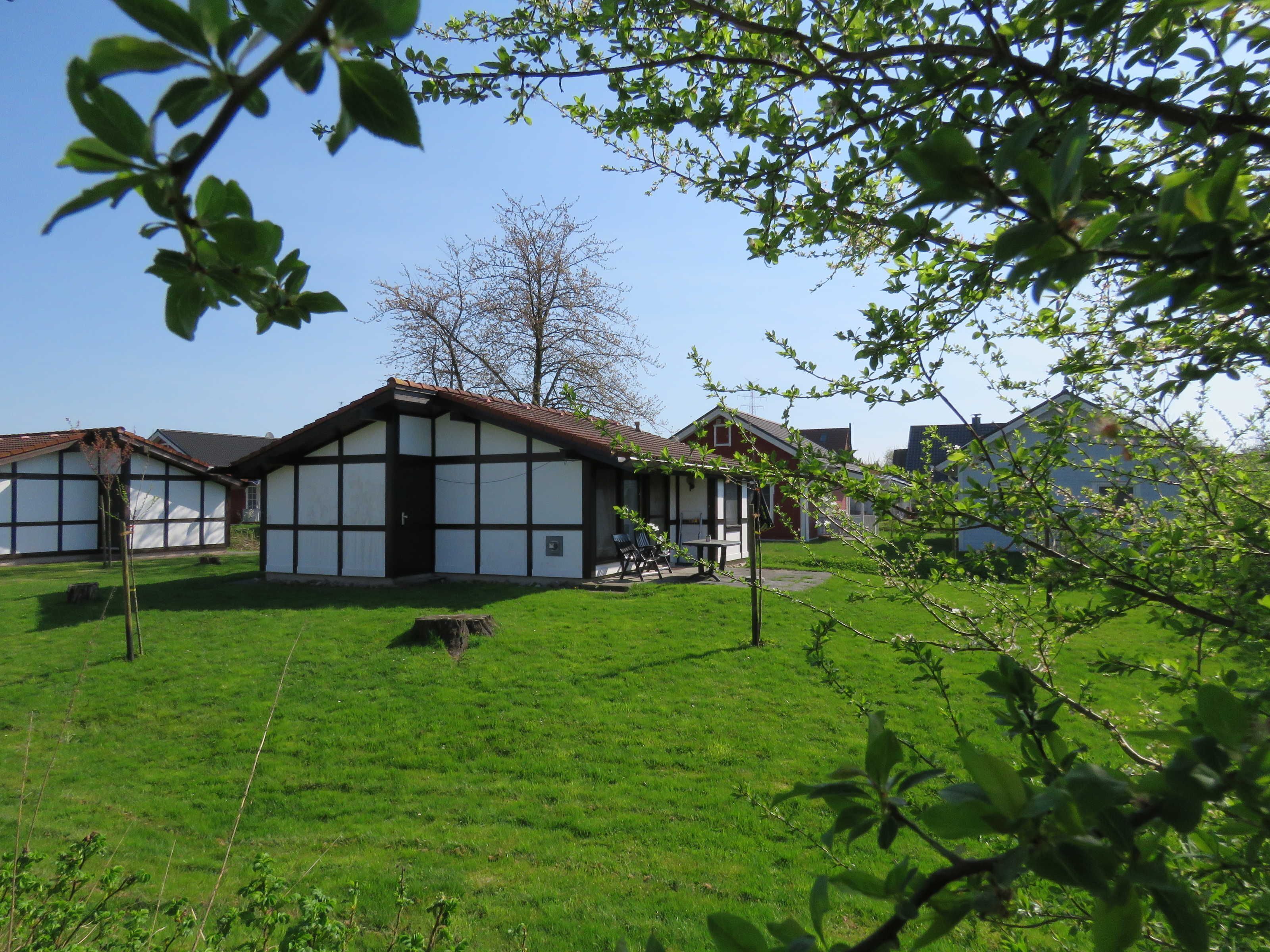 Ein traditionelles Gebäude mit Giebeldach, umgeben von einer grünen Wiese und Bäumen.