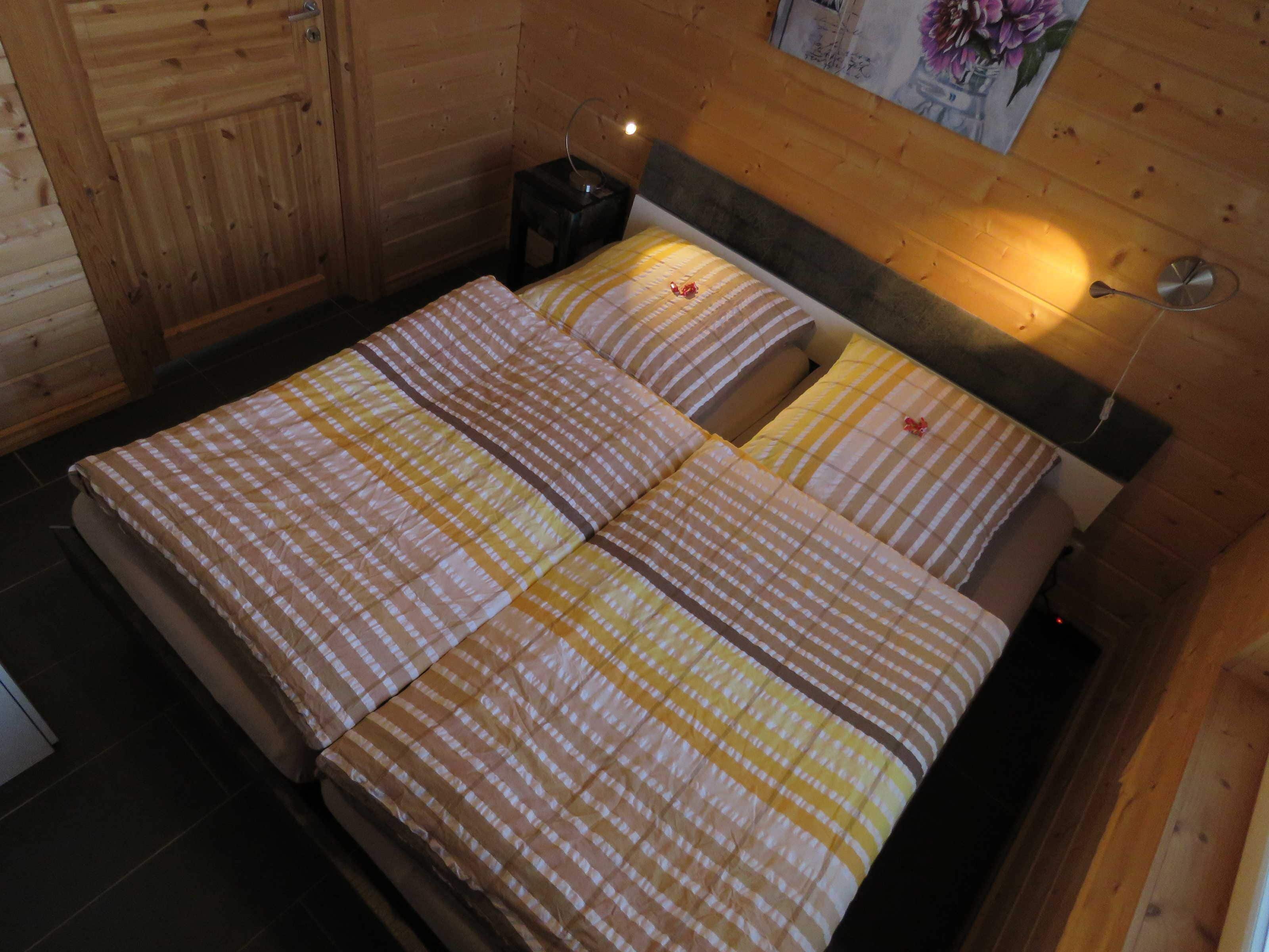 A wooden cabin-style room with a bed, a nightstand, and a wall-mounted lamp.