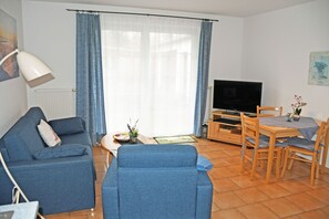 Uma sala de estar com sofá, televisão, mesa de jantar e cadeiras.