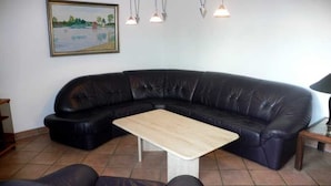 En svart lädersoffa i sektionsmodell med ett träbord i ett rum med kakelgolv.
