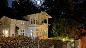 A large, ornate building with multiple windows and a balcony, surrounded by a fence and trees. - a. First floor - Floor - Villa Achterkerke (Heringsdorf)