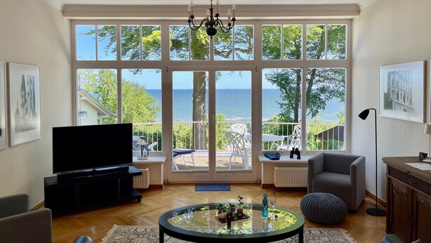A living room with a large window, a television, a round glass table, and a sofa. - a. First floor - Floor - Villa Achterkerke (Heringsdorf)